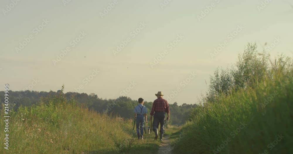 Back view on the grandson with grandfather going to the fishing early in the morning. Outdoor. Back view on the grandson with grandfather going to the fishing early in the morning. Outdoor.