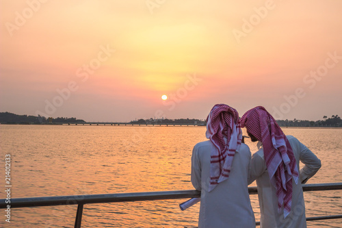 JEDDAH, SAUDI ARABIA - OCTOBER 15, 2016. Two Saudi Arabian men in traditional authentic dress looking on the sunset in Jeddah Corniche near King Fahd's Fountain