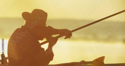 Close up of the old angler in the hat sitting in the boat on the lake and preaparing his road for fishing. Outdoor. photo