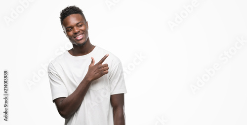 Young african american man wearing white t-shirt cheerful with a smile of face pointing with hand and finger up to the side with happy and natural expression on face looking at the camera.