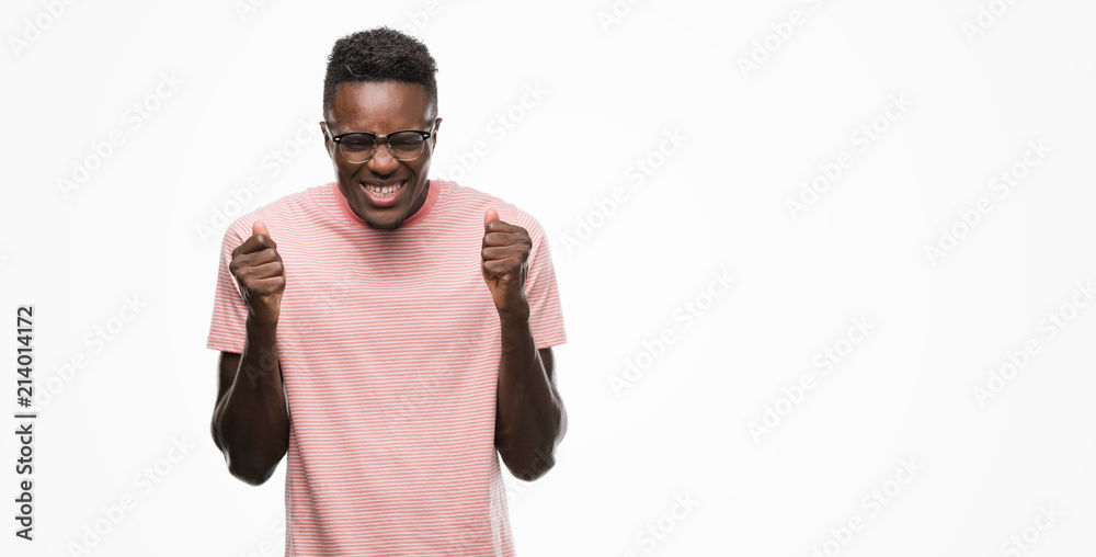 Young african american man wearing pink t-shirt excited for success with arms raised celebrating victory smiling. Winner concept.