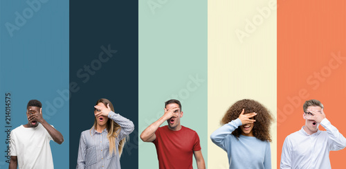 Group of people over vintage colors background peeking in shock covering face and eyes with hand, looking through fingers with embarrassed expression.