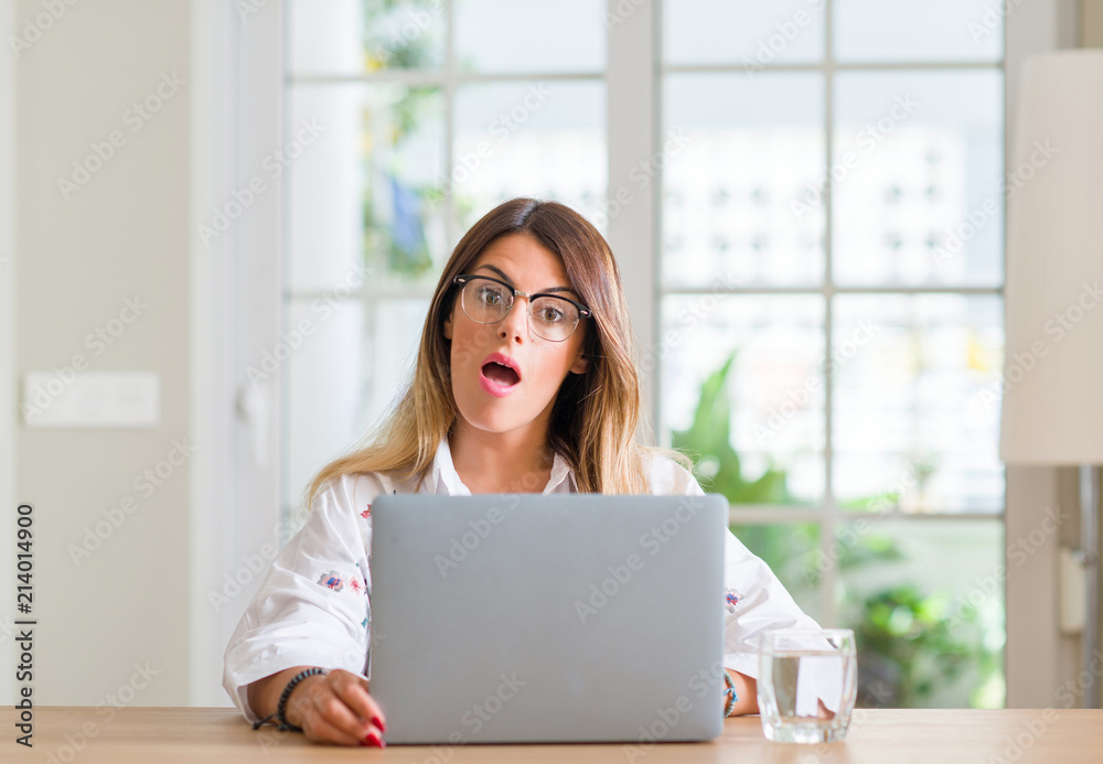 Young woman at home using laptop scared in shock with a surprise face, afraid and excited with fear expression