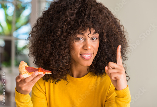 African american woman ready to eat pepperoni pizza slice surprised with an idea or question pointing finger with happy face, number one © Krakenimages.com