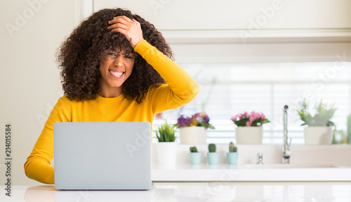 African american woman using computer laptop at kitchen stressed with hand on head, shocked with shame and surprise face, angry and frustrated. Fear and upset for mistake.