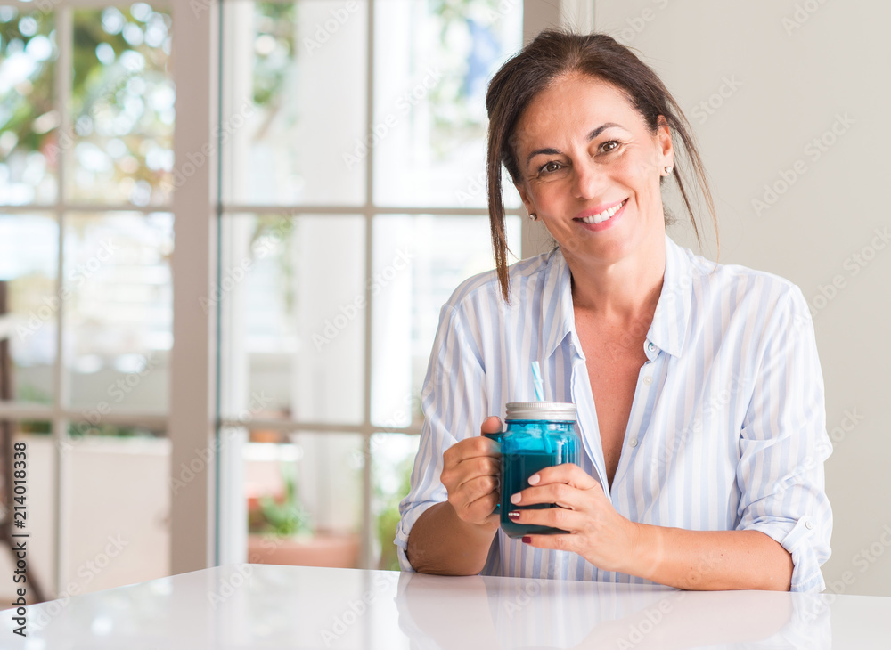 Middle aged woman drinking milk shake in a glass with a happy face standing and smiling with a confident smile showing teeth Middle aged woman drinking milk shake in a glass with a happy face standing and smiling with a confident smile showing teeth