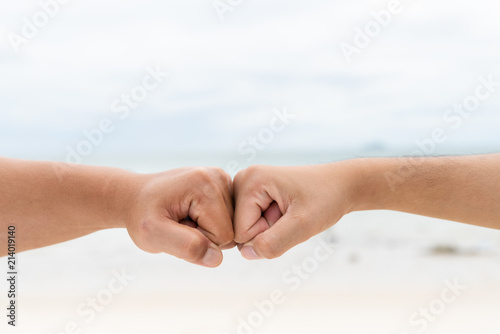 Men hands fist bumping together on blurred sea and sky background. Friendship Day concept.