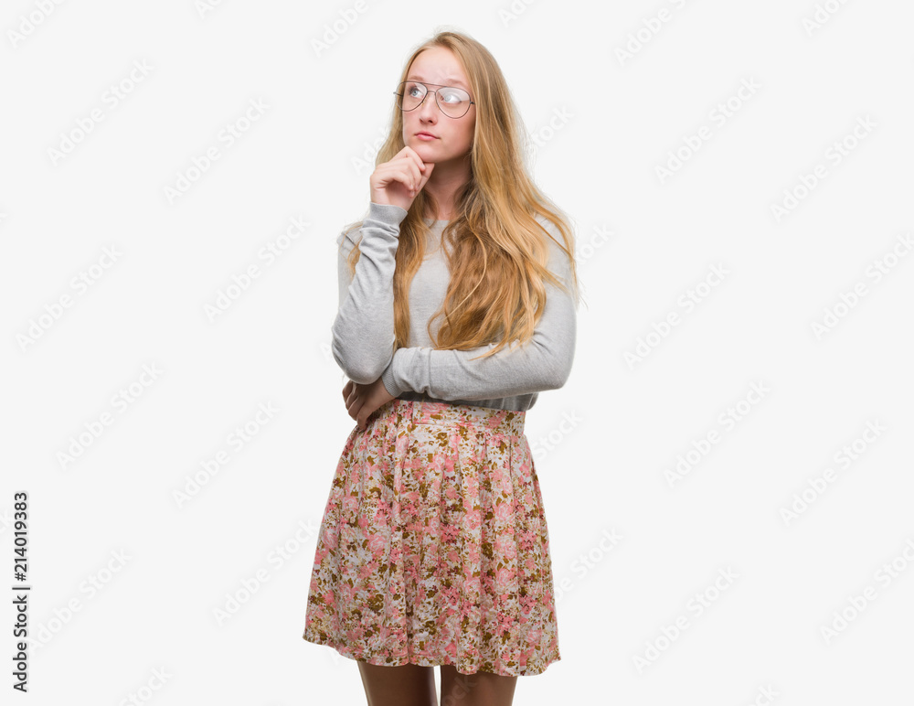Blonde teenager woman wearing flowers skirt with hand on chin thinking about question, pensive expression. Smiling with thoughtful face. Doubt concept. Blonde teenager woman wearing flowers skirt with hand on chin thinking about question, pensive expression. Smiling with thoughtful face. Doubt concept.