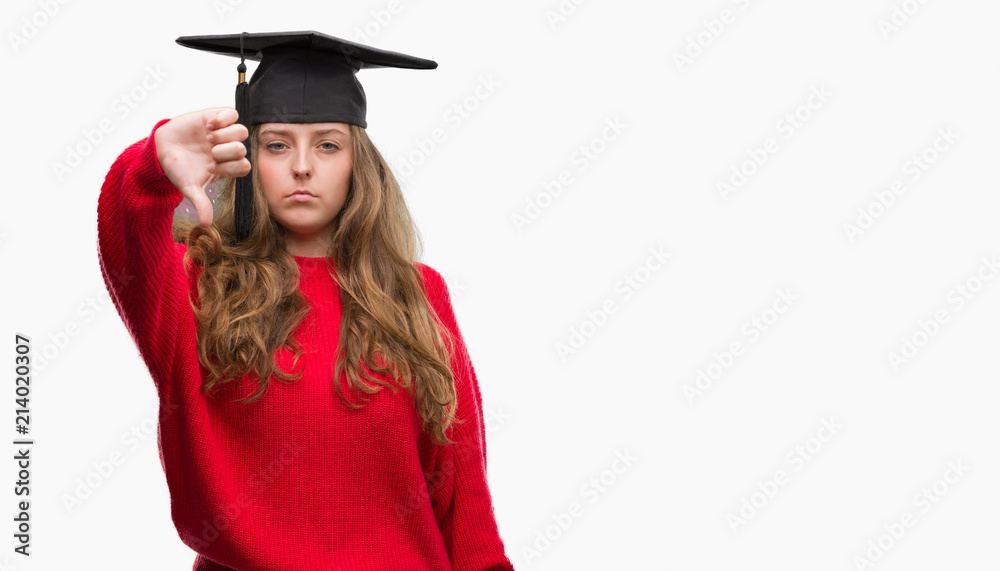 Young blonde woman wearing graduation cap with angry face, negative sign showing dislike with thumbs down, rejection concept Young blonde woman wearing graduation cap with angry face, negative sign showing dislike with thumbs down, rejection concept