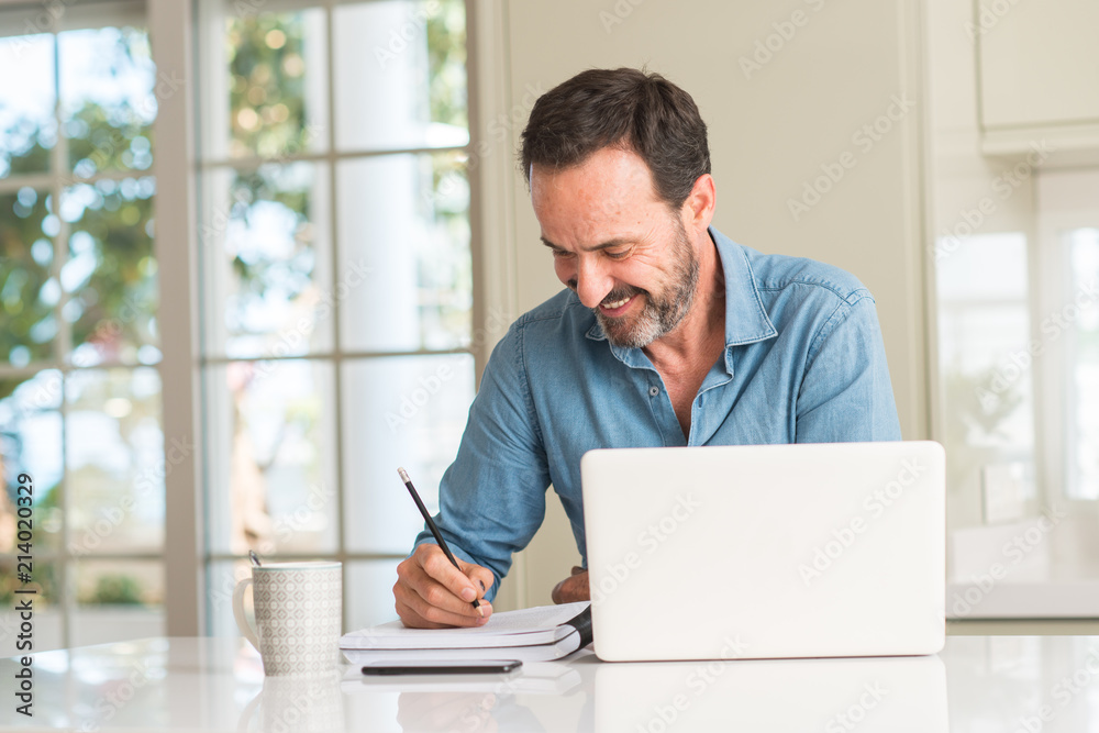 Middle age man using laptop at home with a happy face standing and smiling with a confident smile showing teeth Middle age man using laptop at home with a happy face standing and smiling with a confident smile showing teeth