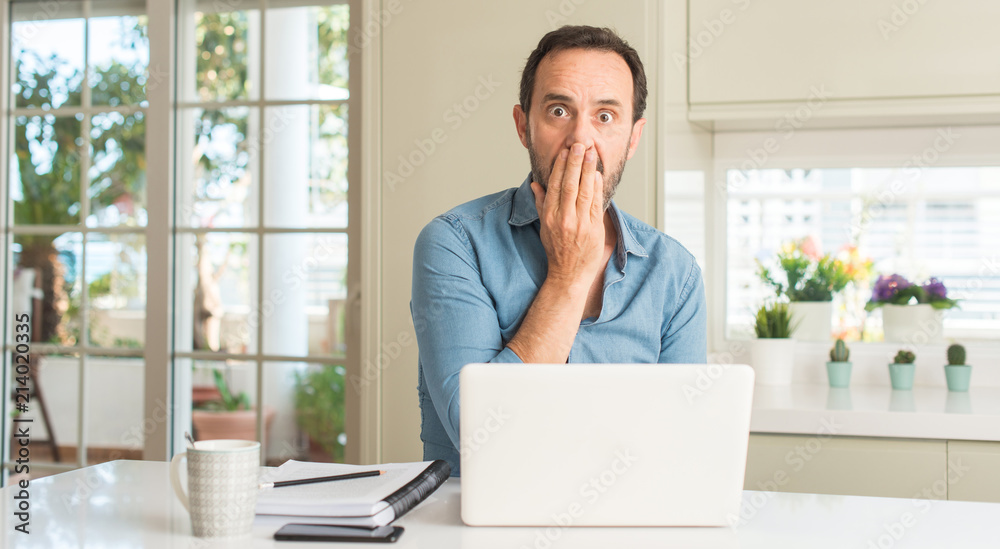 Middle age man using laptop at home cover mouth with hand shocked with shame for mistake, expression of fear, scared in silence, secret concept Middle age man using laptop at home cover mouth with hand shocked with shame for mistake, expression of fear, scared in silence, secret concept
