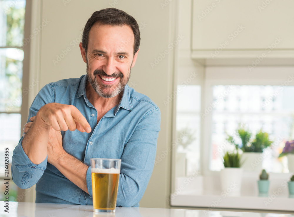 Middle age man drinking beer very happy pointing with hand and finger to the side
