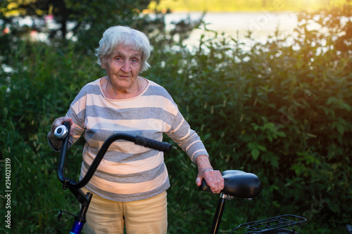 An elderly woman stands with a bicycle. © De Visu