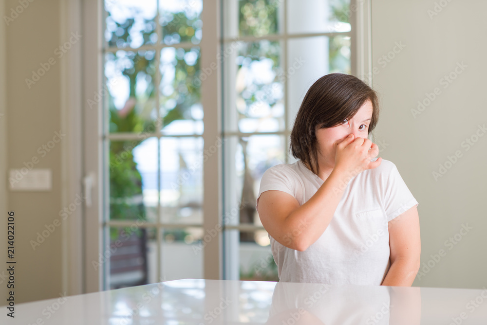 Down syndrome woman at home smelling something stinky and disgusting, intolerable smell, holding breath with fingers on nose. Bad smells concept. Down syndrome woman at home smelling something stinky and disgusting, intolerable smell, holding breath with fingers on nose. Bad smells concept.