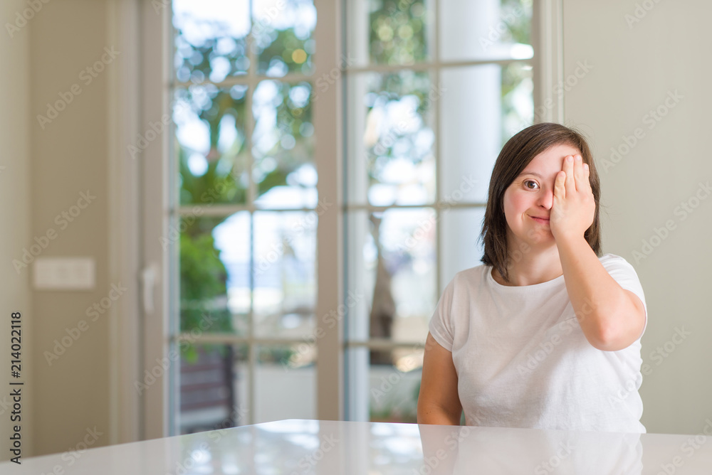 Down syndrome woman at home covering one eye with hand with confident smile on face and surprise emotion. Down syndrome woman at home covering one eye with hand with confident smile on face and surprise emotion.