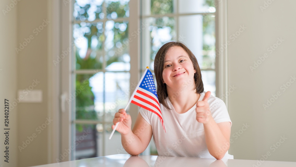 Down syndrome woman at home holding flag of usa happy with big smile doing ok sign, thumb up with fingers, excellent sign