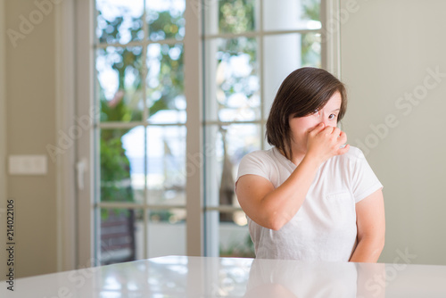 Down syndrome woman at home smelling something stinky and disgusting, intolerable smell, holding breath with fingers on nose. Bad smells concept.
