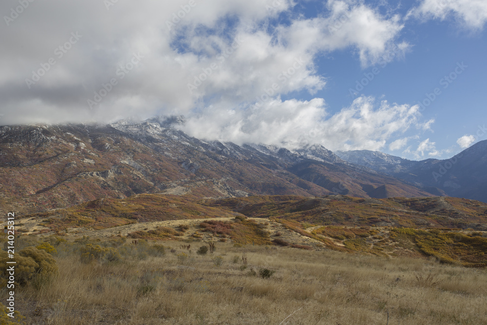Panoramic view of mountains with short grass field upfront. Fall colors. Snow on top of mountains.