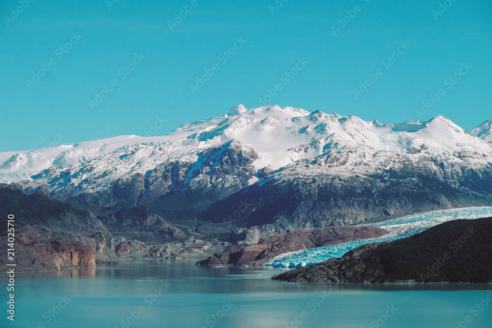 The blue glacier descends to a large lake in the background of snow-capped mountains