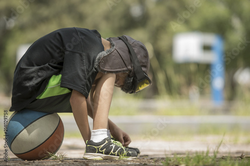 lonely child in a pilot aviator hat, with an attitude of shame, guilt, boredom, sitting on a basketball while adults have fun on other less important things like watching their facebook