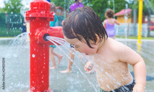 Happy toddler boy playing in water park spray ground