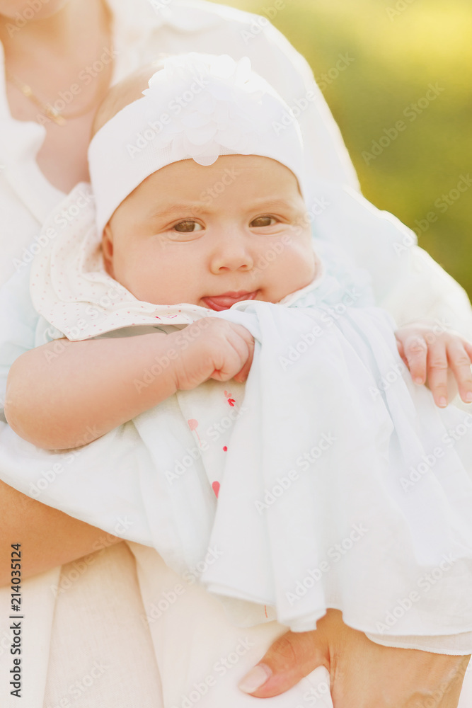 Close up cropped shot of half-year little baby girl in arms of sweet mommy. Cute child looking at camera. Soft sun light picture. Happy family spend time together in summer, white clothes Close up cropped shot of half-year little baby girl in arms of sweet mommy. Cute child looking at camera. Soft sun light picture. Happy family spend time together in summer, white clothes