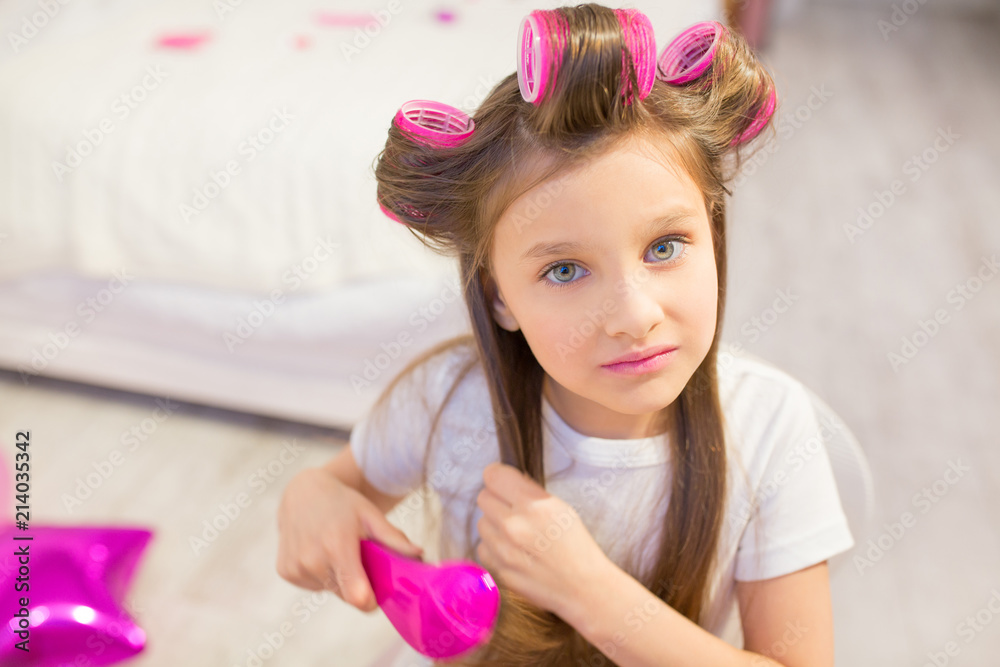 Cute preschooler taking care of her hair. Dreamy little girl wearing white tee brushing her hair with pink hairbrush and looking up. Cute preschooler taking care of her hair. Dreamy little girl wearing white tee brushing her hair with pink hairbrush and looking up.