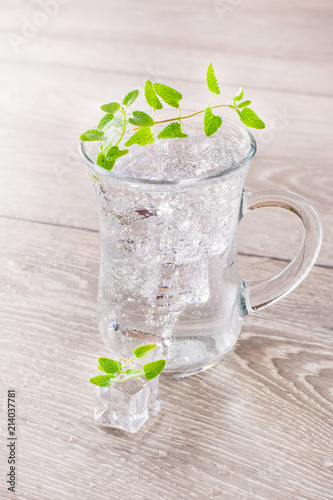 Cold mineral water with ice cubes and mint leaves in a transparent glass on a wooden table