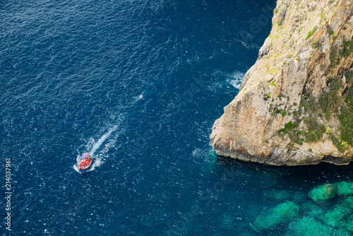 A typical boat pass around the steep rock of Blue Grotto of Malta, aerial view.