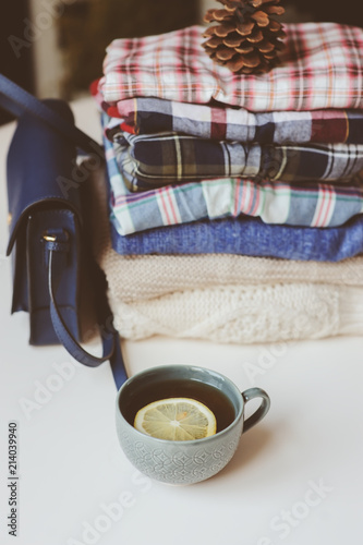 fall casual woman fashion clothes set. Stack of plaid shirts and knitted sweaters with pine cone and cup of tea. Cozy stylish womanswear and hygge concept. photo