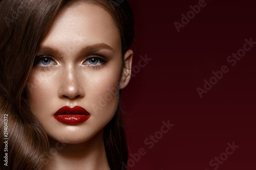 A beautiful girl with evening make-up, a curls wave and red lips. Beauty face. Photo taken in the studio.