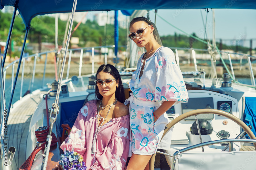 Two young attractive women are resting on a yacht on a Sunny day . Beautiful women in fashionable summer clothes on a yacht