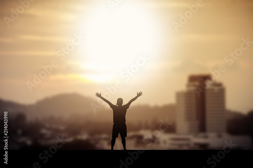 Man holding arms up in praise to God against sunrise at morning with city and vintage background.