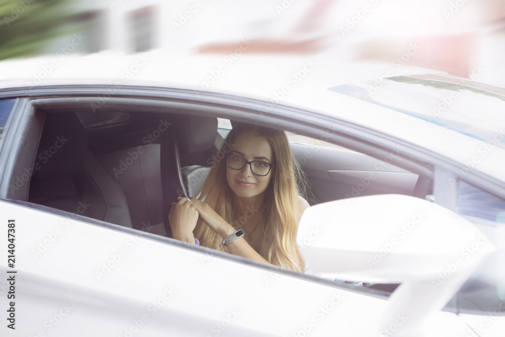 smiling, beautiful girl blond in glasses with an expensive white car on the road is standing