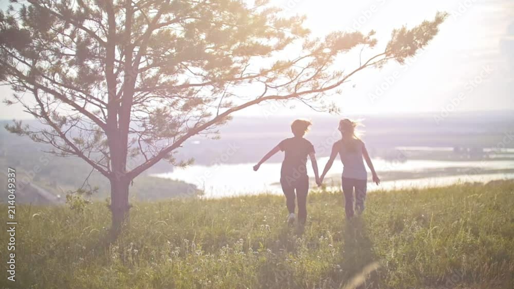 Two young women holding hands running on the hill at sunset Two young women holding hands running on the hill at sunset