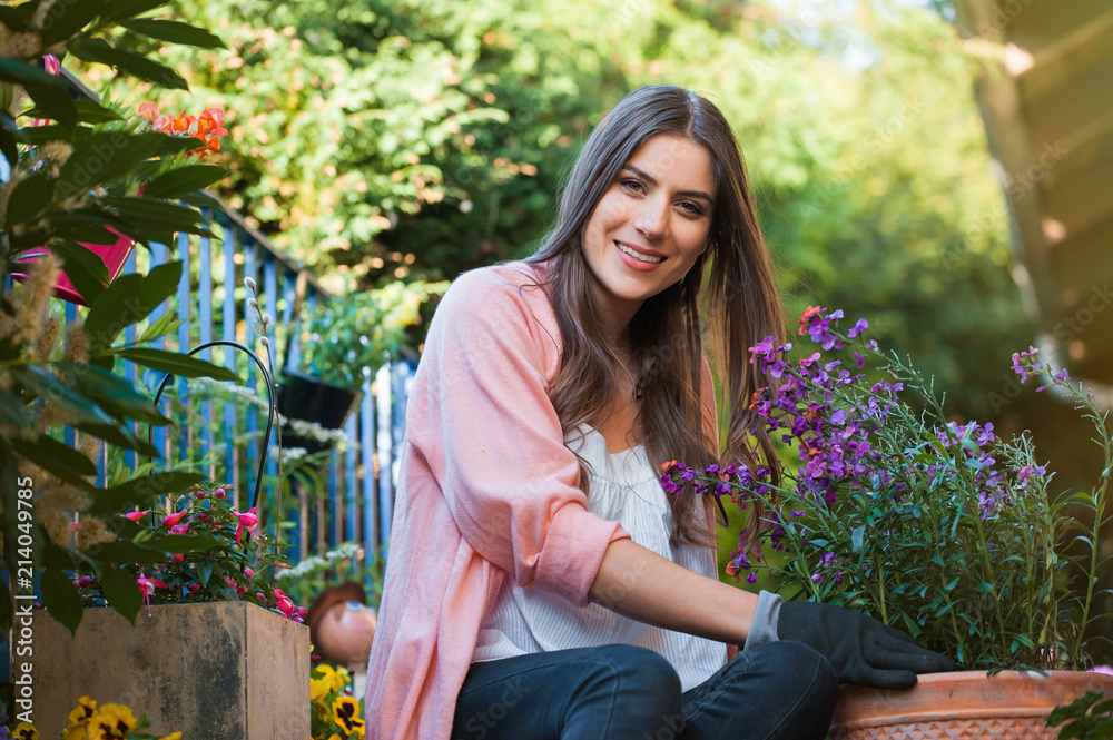 Pretty young girl smiling and gardening in pots on the terrace,at home, with working gloves. Gardening as hobby and leisure concept.