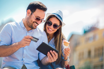 Happy couple paying on line with credit card and digital tablet on the street
