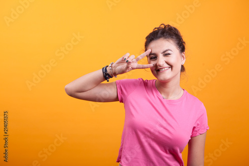 Beautiful young woman being victorius with pink t-shirt over yellow background in studio
