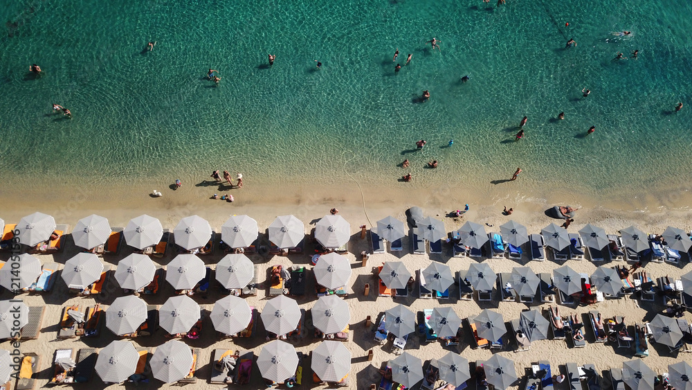 Aerial drone, bird's eye view photo of famous crowded full of sun beds turquoise colour sandy beach of Ornos, Mykonos island, Cyclades, Greece