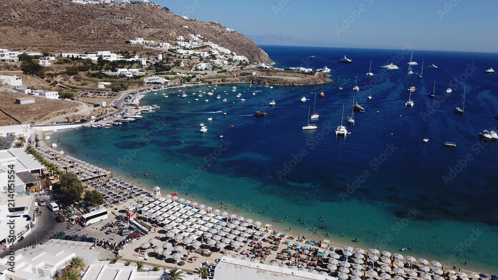 Aerial drone bird's eye view photo of famous organized with sun beds crystal clear water beach of Ornos in island of Mykonos, Cyclades, Greece