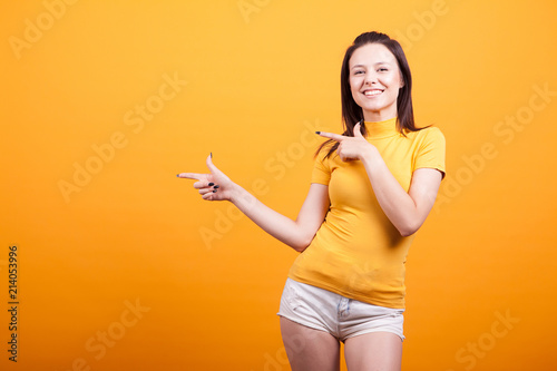 Cute young woman pointing in studio on yellow background