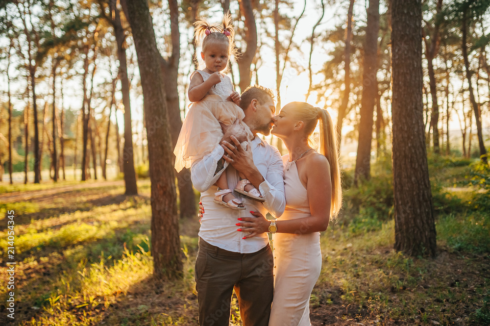 Beautiful mother and father hug daughter in the forest background. Happy family in vacation and travel. Mom show to her child something away. Caucasian family Beautiful mother and father hug daughter in the forest background. Happy family in vacation and travel. Mom show to her child something away. Caucasian family