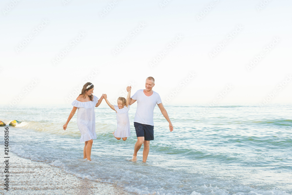 Parents run along the sea beach with daughter.