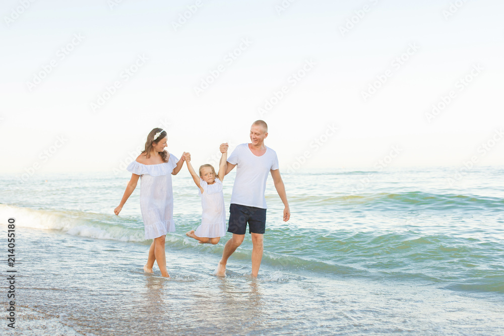 Young parents walk along the seashore with daughter .