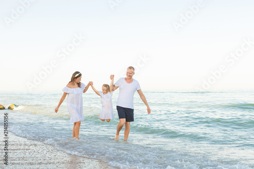 Parents run along the sea beach with daughter.