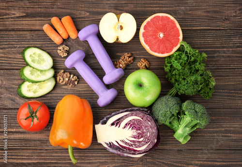 Flat lay composition with fresh vegetables, fruits and dumbbells on wooden background. Diet food