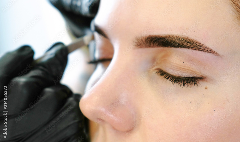 Cosmetologist performs the procedure of correction eyebrow with tweezers. Front closeup view.