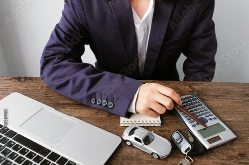 Businessman is calculating car purchase cost with calculator ,laptop ,car model ,key and blank notebook on wooden table..