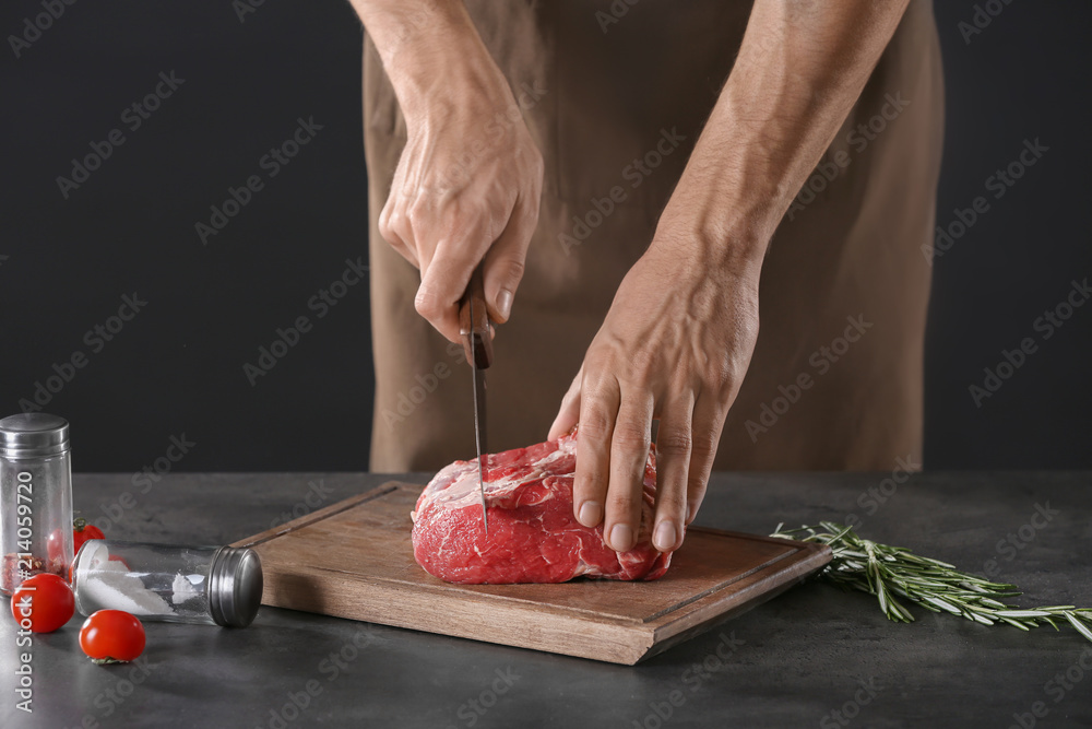 Man cutting fresh raw meat on wooden board