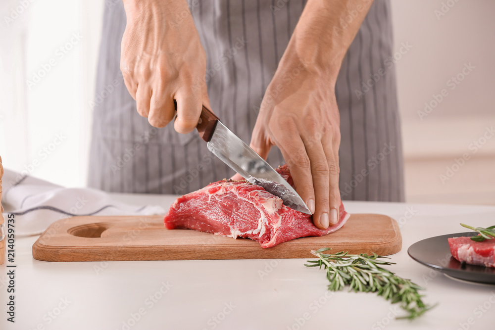 Man cutting fresh raw meat on wooden board in kitchen